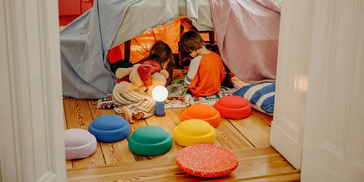 Children reading in a cosy blanket den, surrounded by Stapelstein limited edition Hidden Giants stepping stones