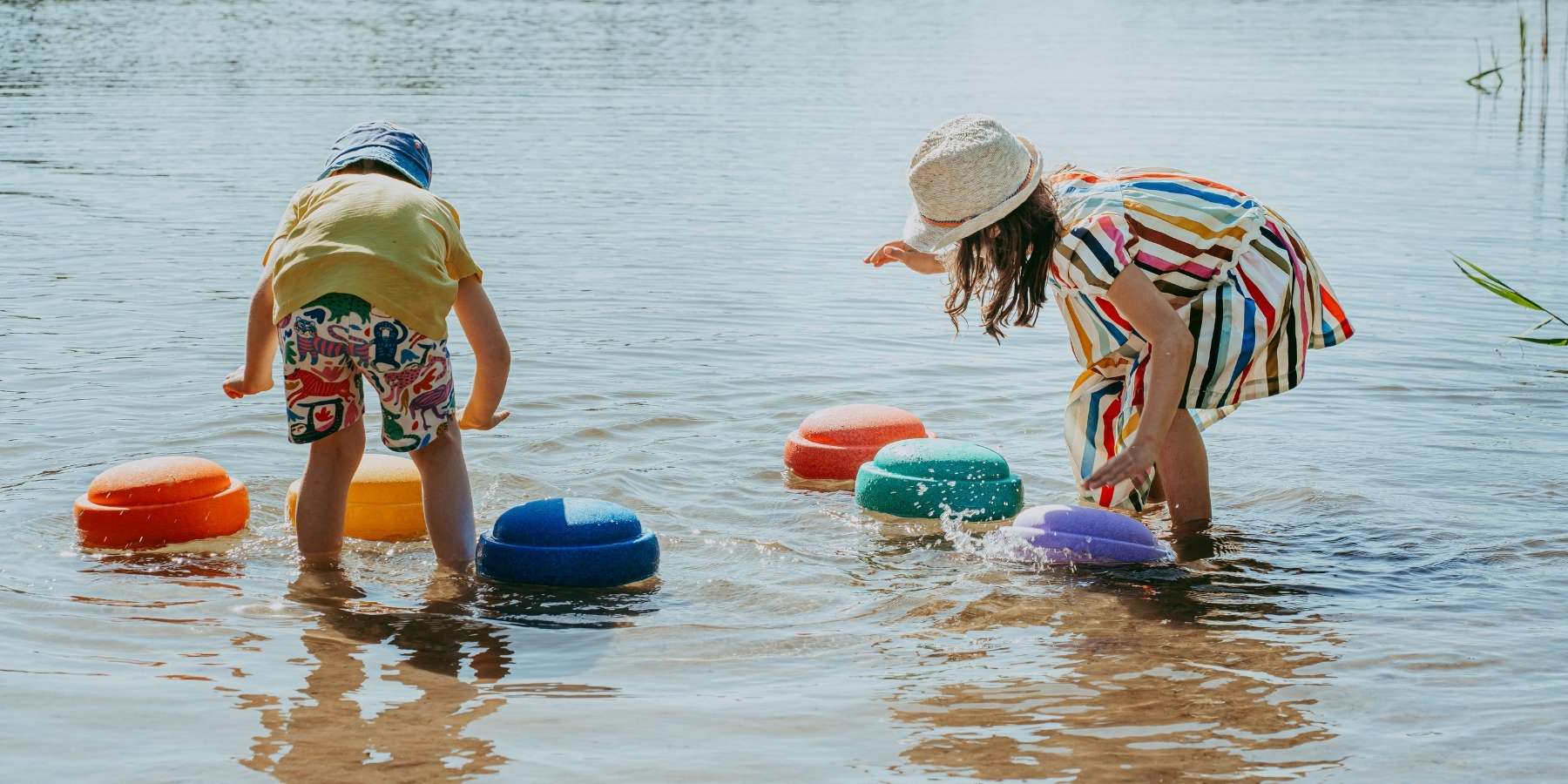 Two children playing with colourful Stapelstein stones in a body of water.