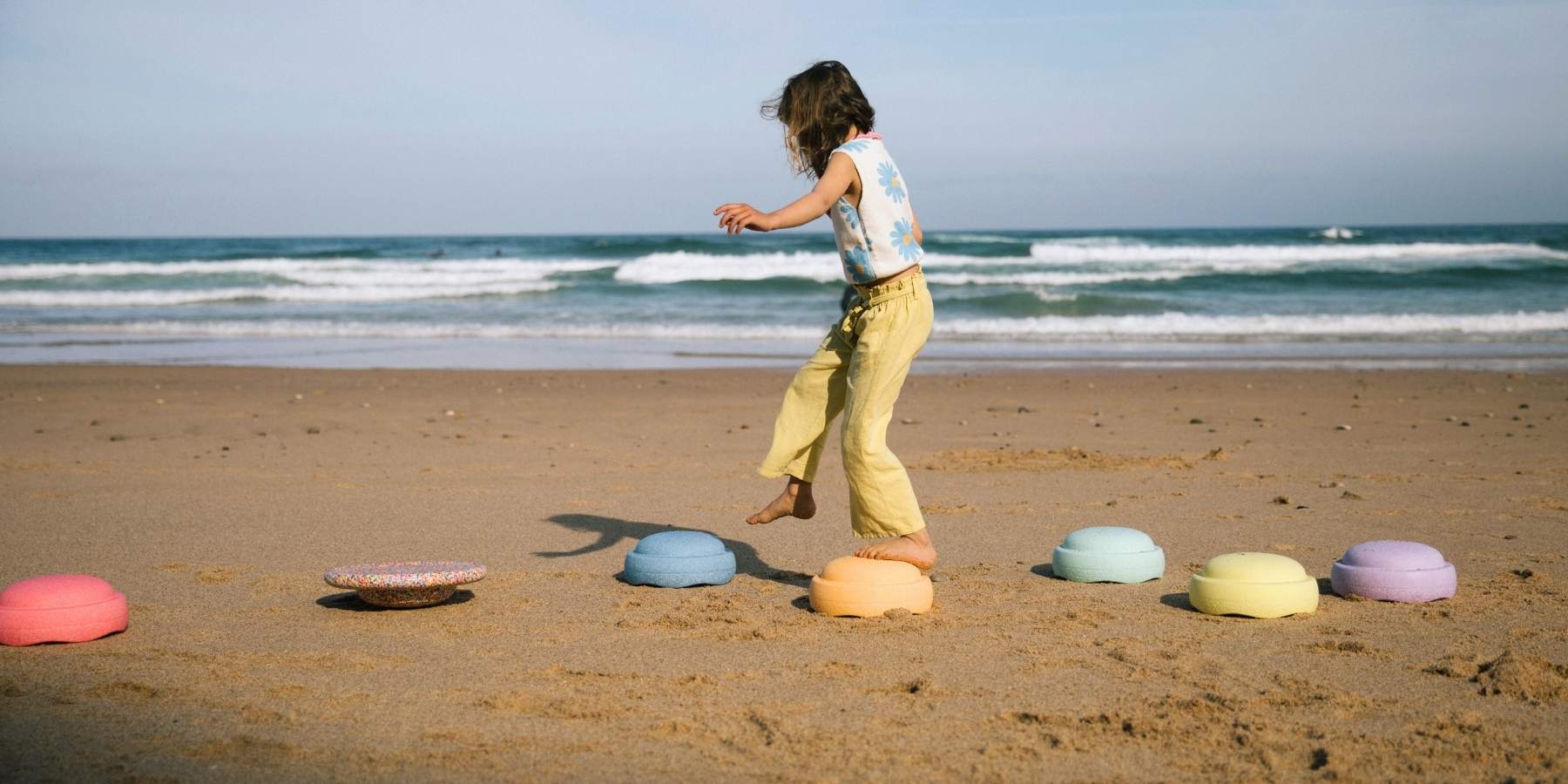 Child playing on a beach with colourful Stapelstein stepping stones