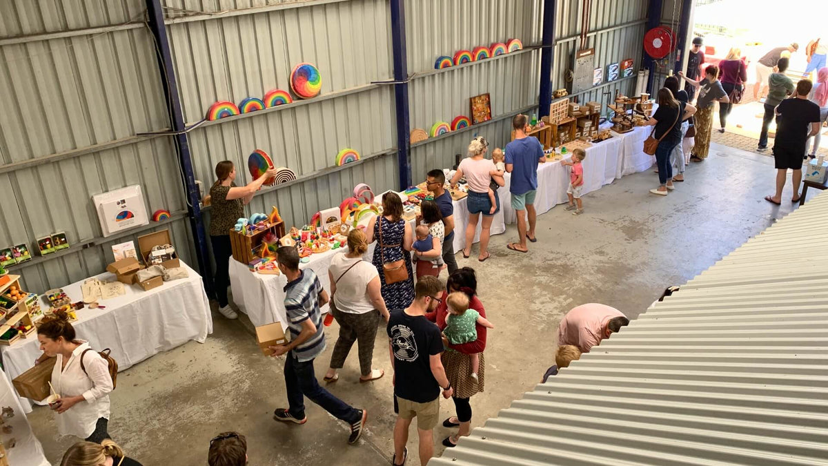 Customers shopping at an Oskar's Wooden Ark warehouse open day with tables displaying various wooden toys.