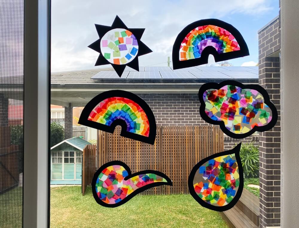 Finished rainbow paper sun catchers displayed on a window, catching sunlight to create a stained glass effect