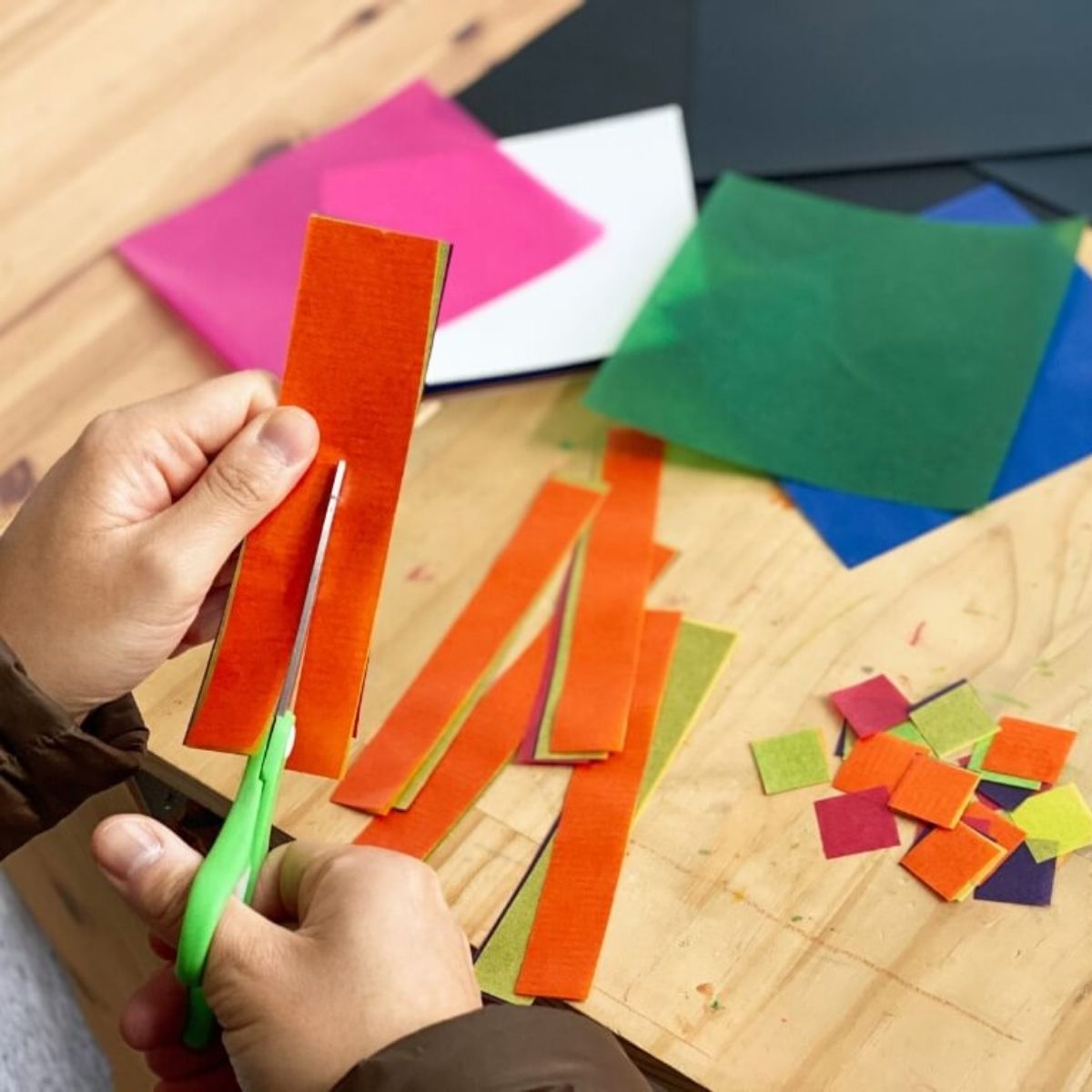 A child making a sun catcher with colourful waxed kite paper strips on sticky contact shapes.