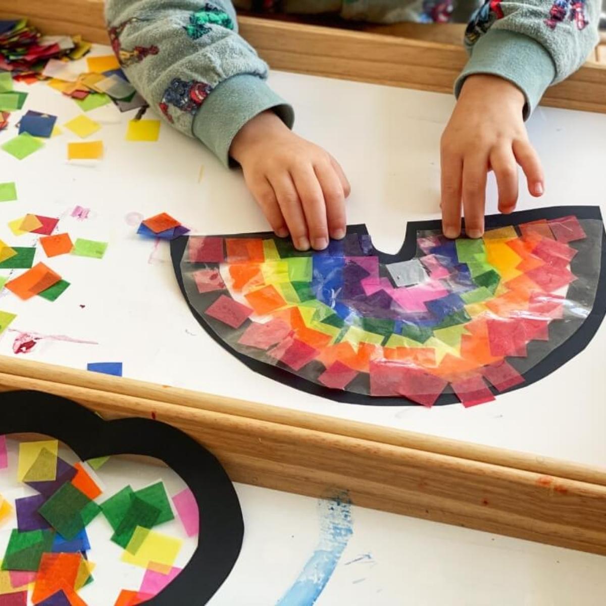 A child making a sun catcher with colourful waxed kite paper squares on sticky contact shapes.