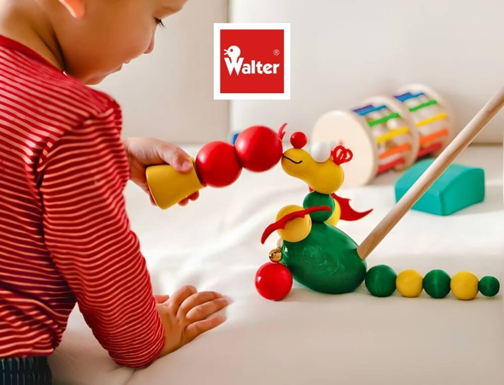 Walter Wooden Toys lifestyle image with logo, featuring a toddler playing with a colourful wooden toy dragon on a white surface – Oskar's Wooden Ark