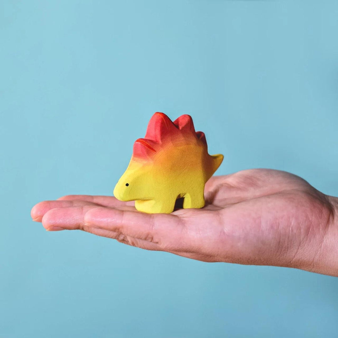 BumbuToys Handcrafted Wooden Dinosaur Baby Stegosaurus from Australia on an adult person's hand