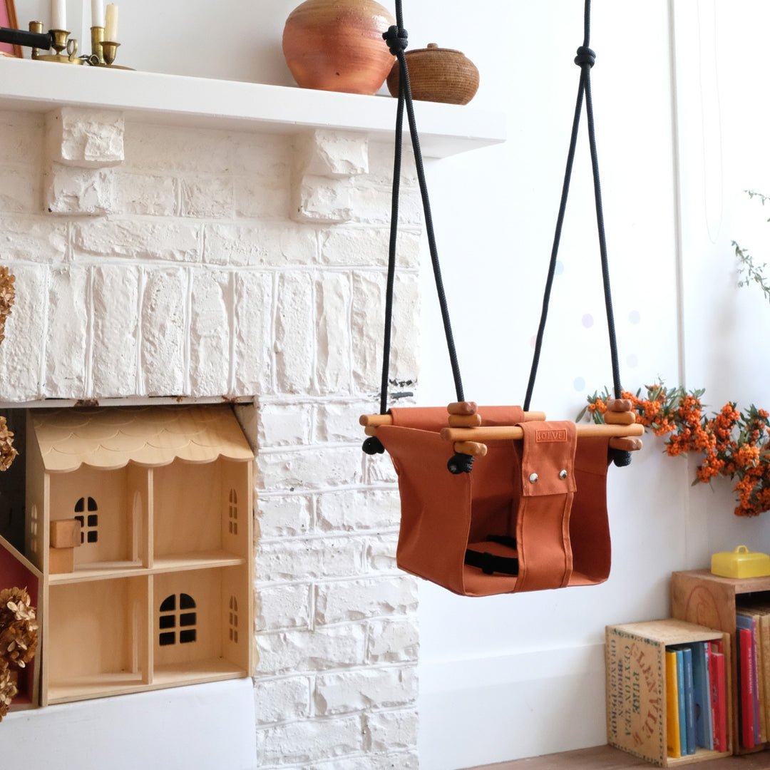 Autumn Rust SOLVEJ Convertible Baby & Toddler Swing hung indoors in a child's play room