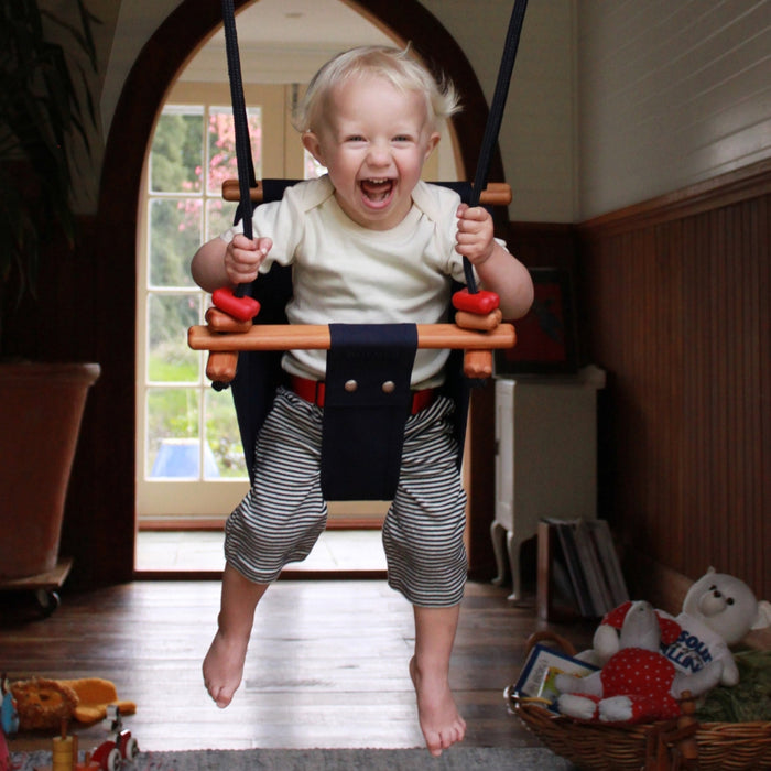 A happy toddler boy swinging indoors using Midnight Blue SOLVEJ Convertible Baby & Toddler Swing from Australia
