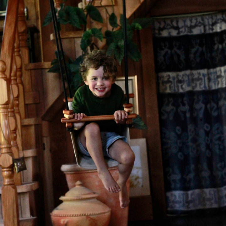 A boy swinging indoors using SOLVEJ Convertible Baby & Toddler Swing from Australia