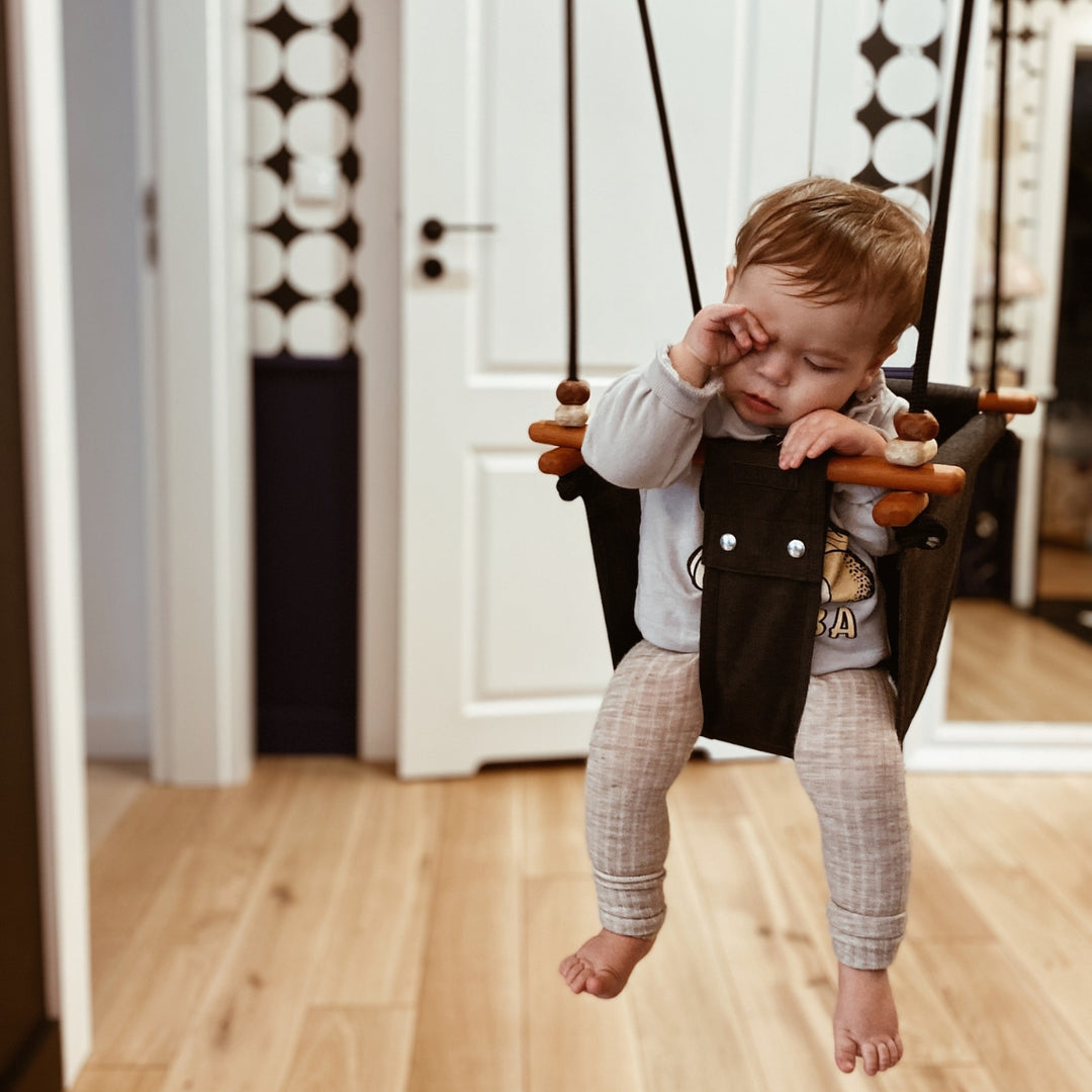 A sleepy baby on SOLVEJ Convertible Baby & Toddler Swing hung indoors
