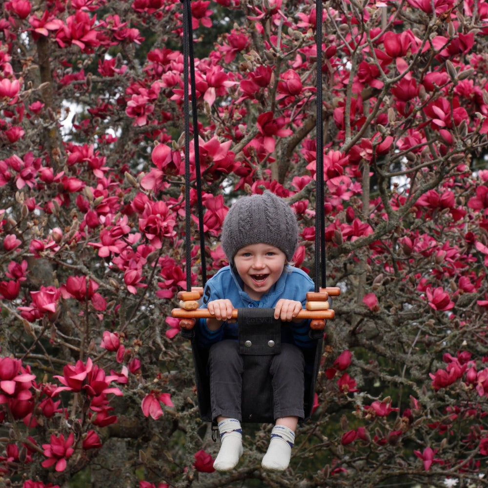 A happy toddler boy swinging outdoors using Coral Black SOLVEJ Convertible Baby & Toddler Swing from Australia