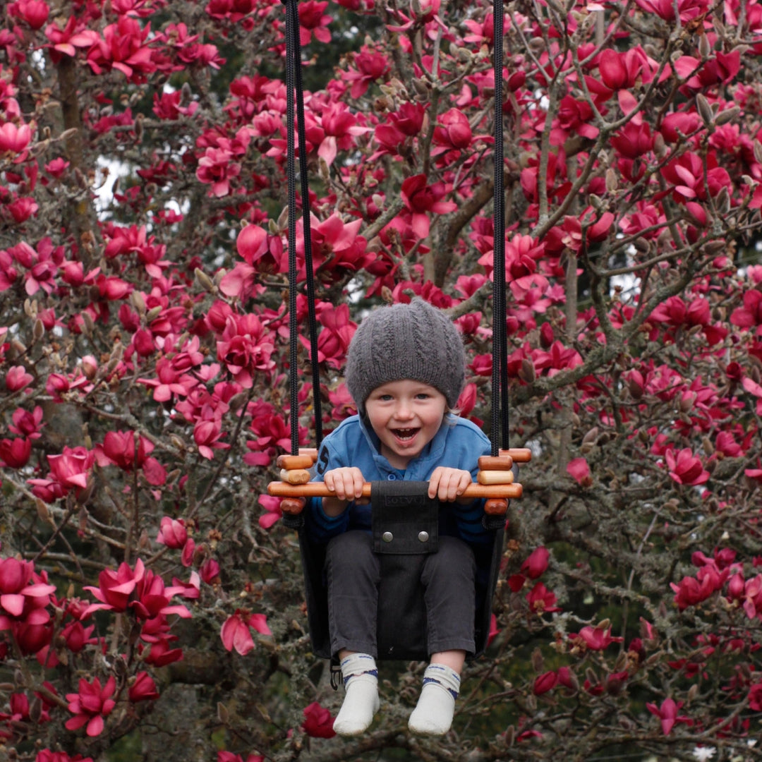 A happy toddler boy swinging outdoors using Coral Black SOLVEJ Convertible Baby & Toddler Swing from Australia