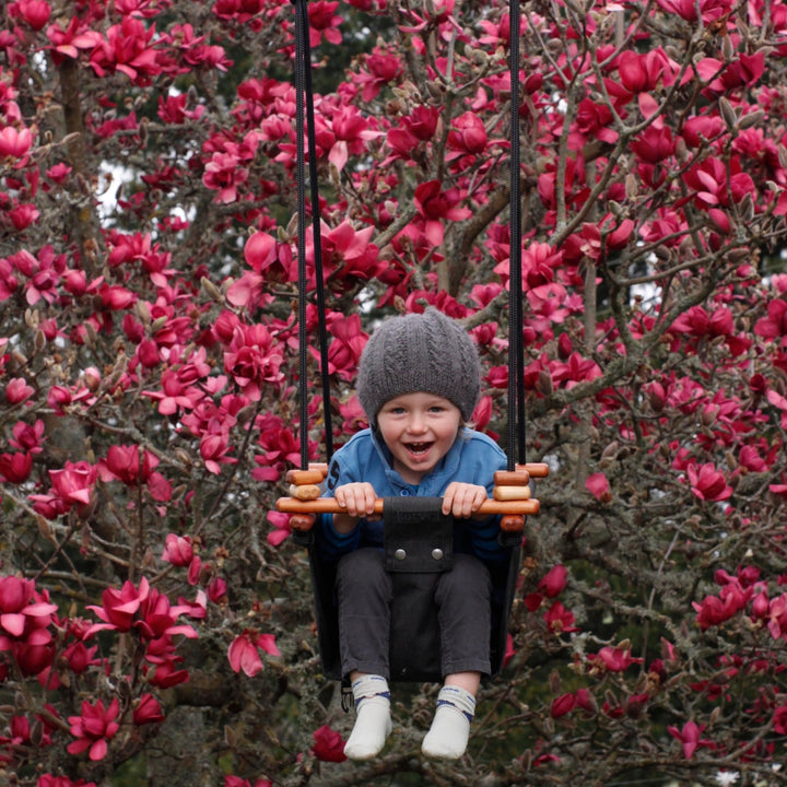 A happy toddler boy swinging outdoors using Coral Black SOLVEJ Convertible Baby & Toddler Swing from Australia