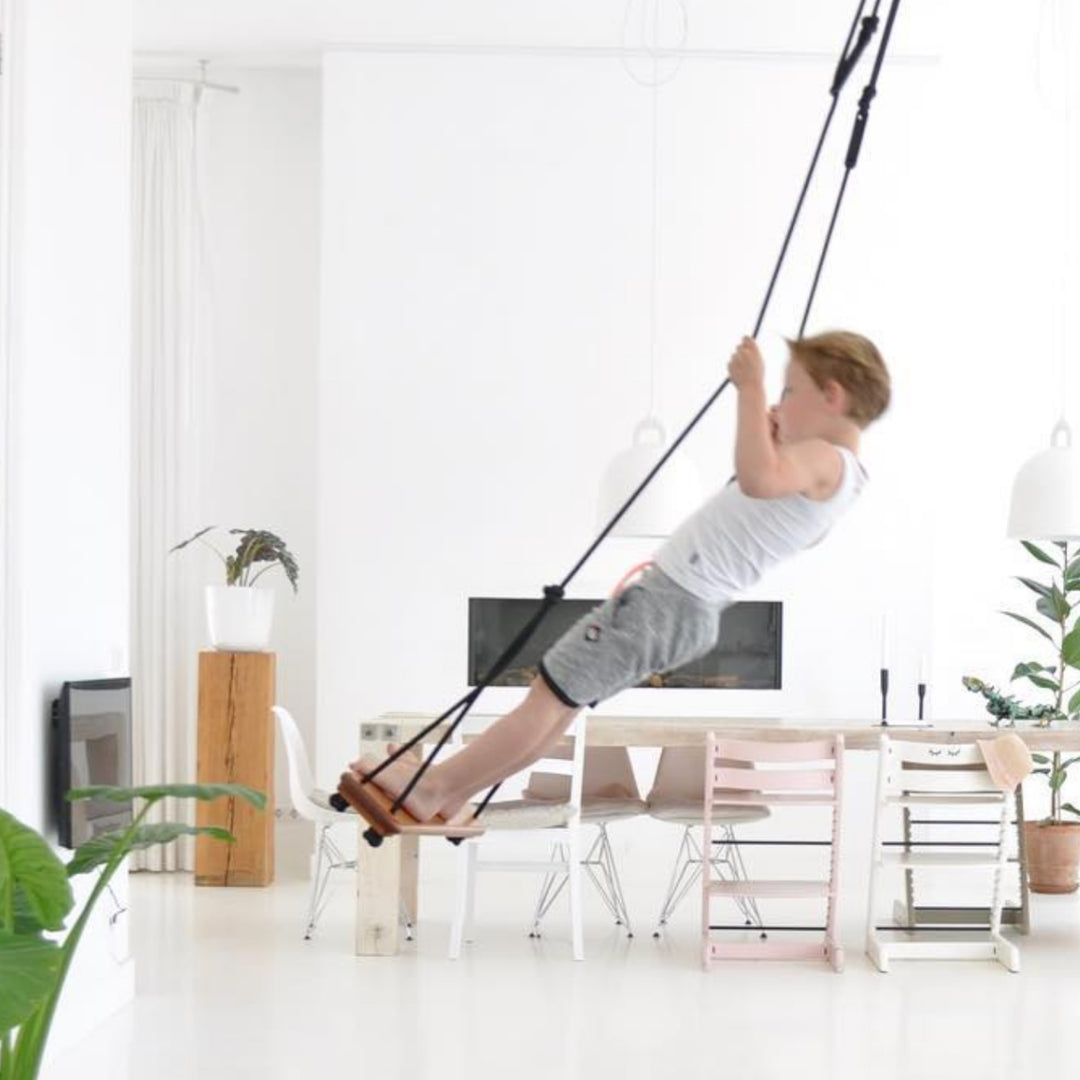A boy doing a play swing trick indoors using SOLVEJ Traditional Wooden Board Swing with Black Rope from Australia