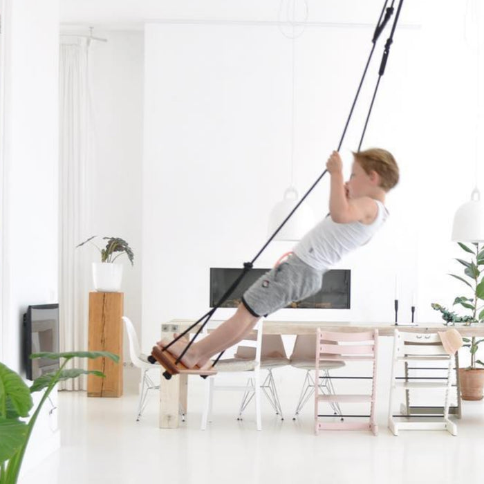 A boy doing a play swing trick indoors using SOLVEJ Traditional Wooden Board Swing with Black Rope from Australia