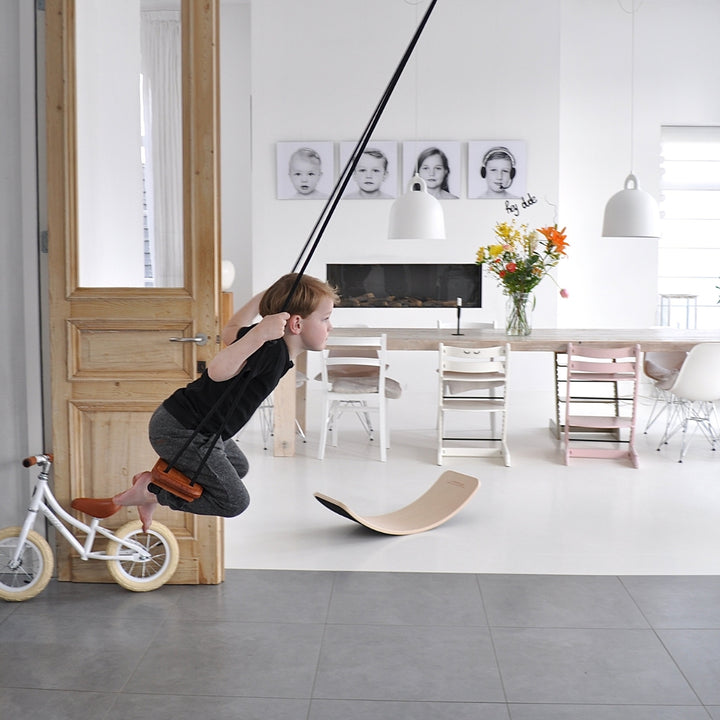 A boy swinging indoors using  SOLVEJ Traditional Wooden Board Swing with Black Rope from Australia