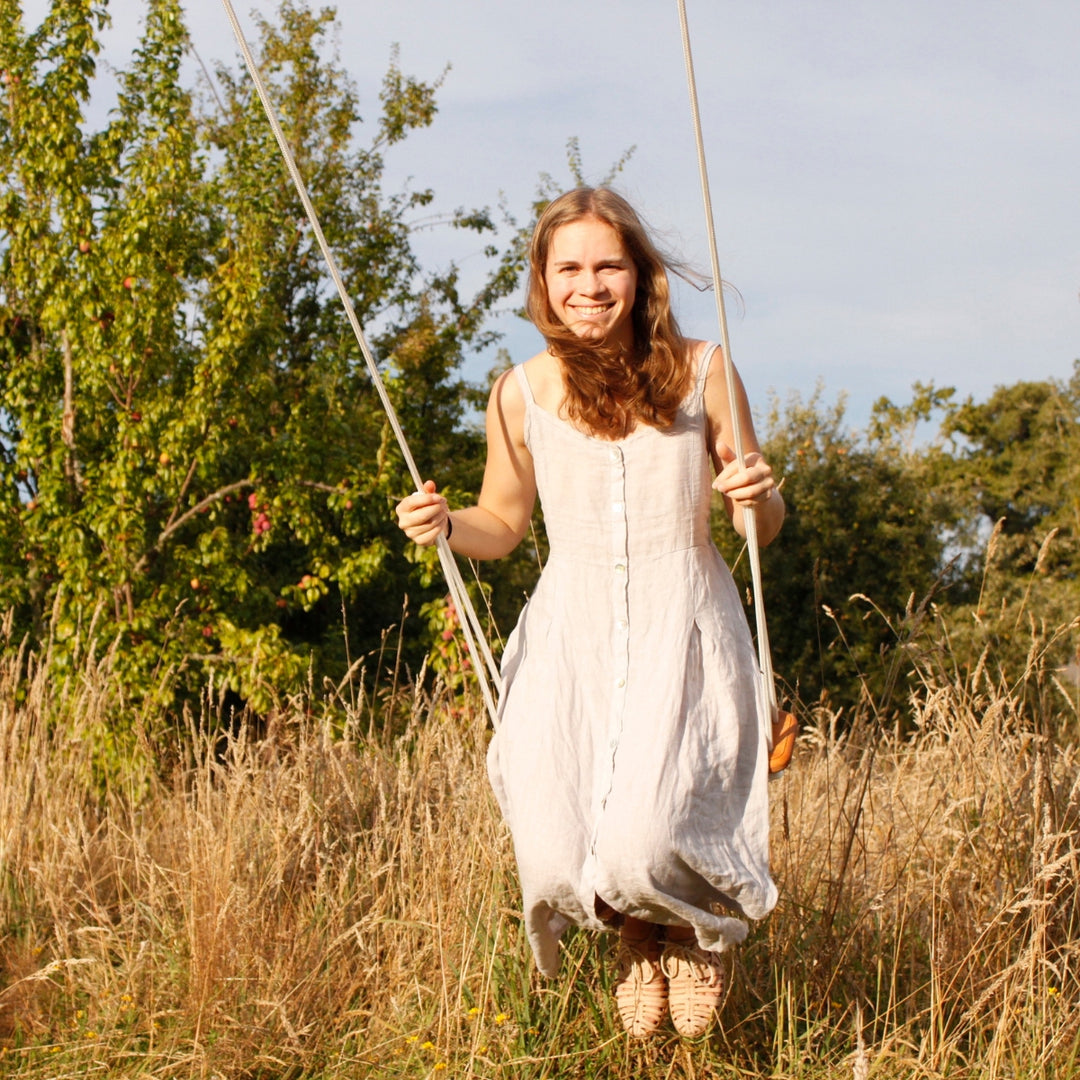 A woman smiling while swinging outdoors on the SOLVEJ Wooden Traditional Board Swing with White Rope from Australia