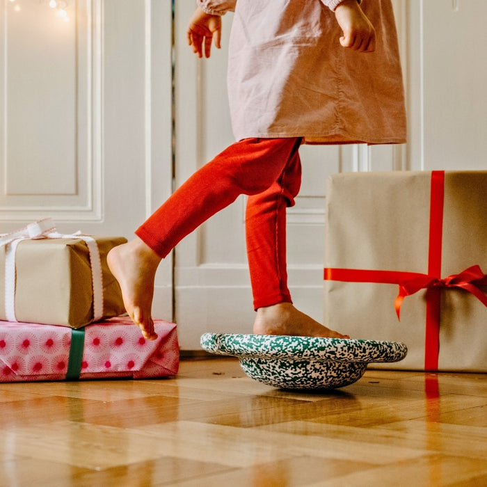 Child in red pants stepping on stepping stones with wrapped gifts on the floor