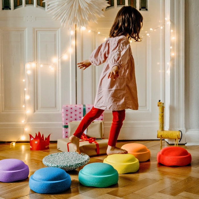 Child playing with colorful stools in a room decorated with string lights